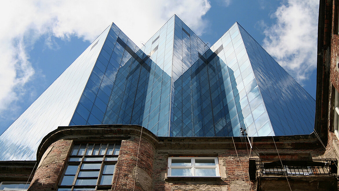 Blick von unten auf modernes Hochhaus aus Glas hinter alter Backsteinfassade.