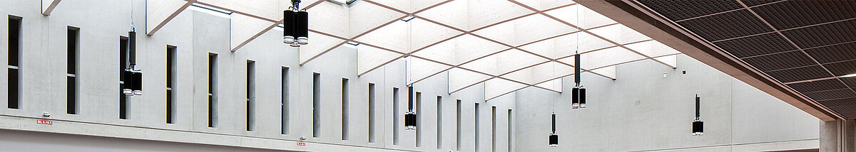 Modernes Atrium im Willibald-Gluck-Gymnasium in Neumarkt mit LAMILUX Glasdach, Betonwänden und farbigen Böden.