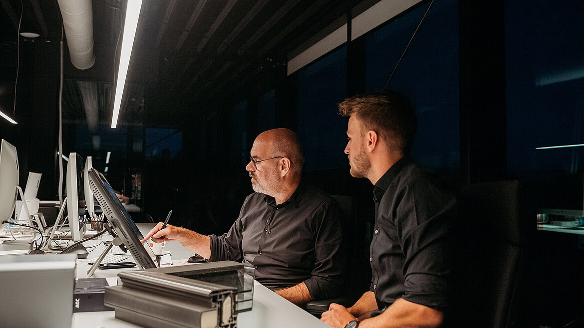 Zwei Männer sitzen am Tisch mit Laptop und arbeiten konzentriert