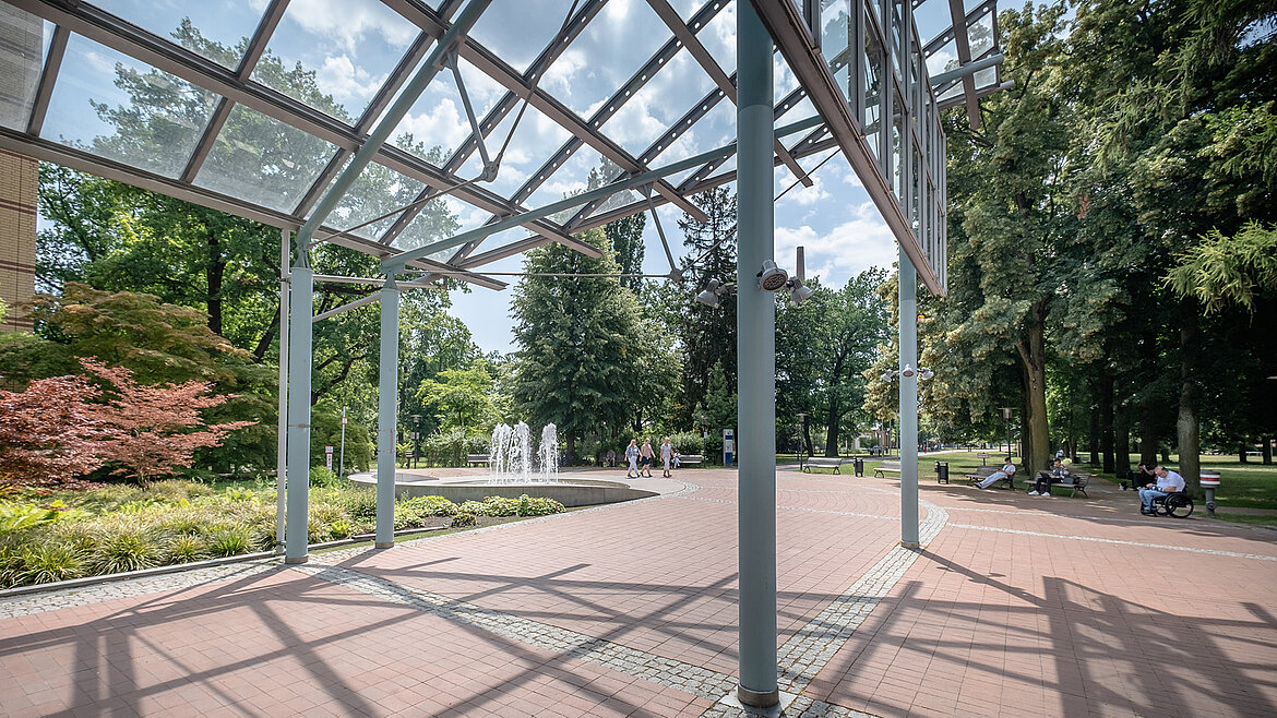 Überdachte Außenfläche mit filigraner Stahl-Glas-Konstruktion im Park.