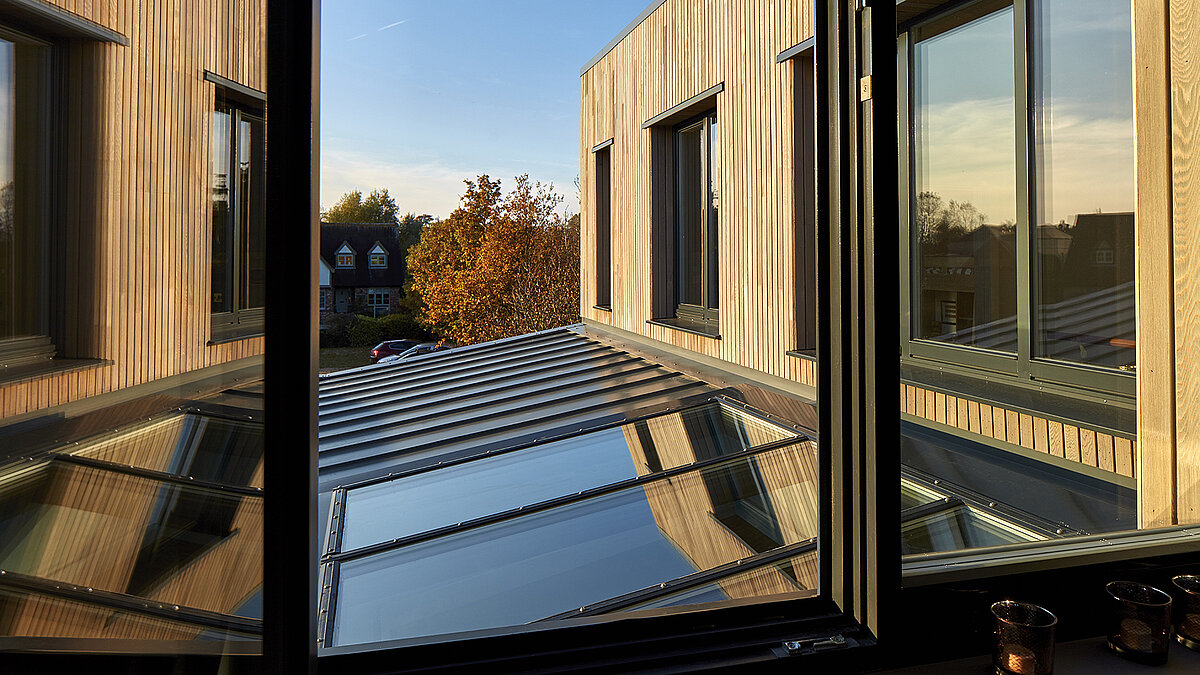 Blick aus einem Fenster auf das Glasdach und die Fassade des Potton Show Homes in England bei warmem Sonnenlicht.