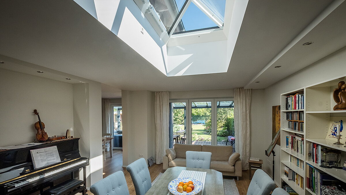 Wohnzimmer in einem Wohnhaus in Hamburg mit LAMILUX Flachdachfenster FW, das natürliches Licht auf den Esstisch und die Bücherregale wirft.