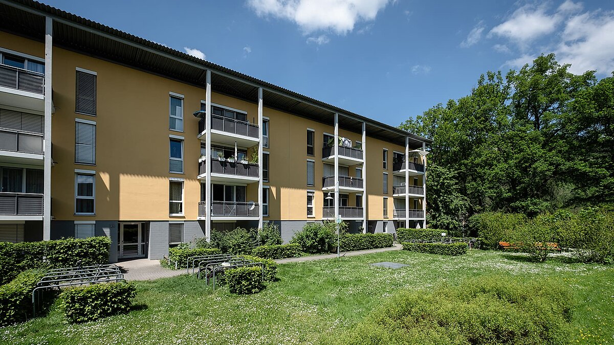 Mehrfamilienhaus in Freiburg mit gelber Fassade, Balkonen und grüner Außenanlage.