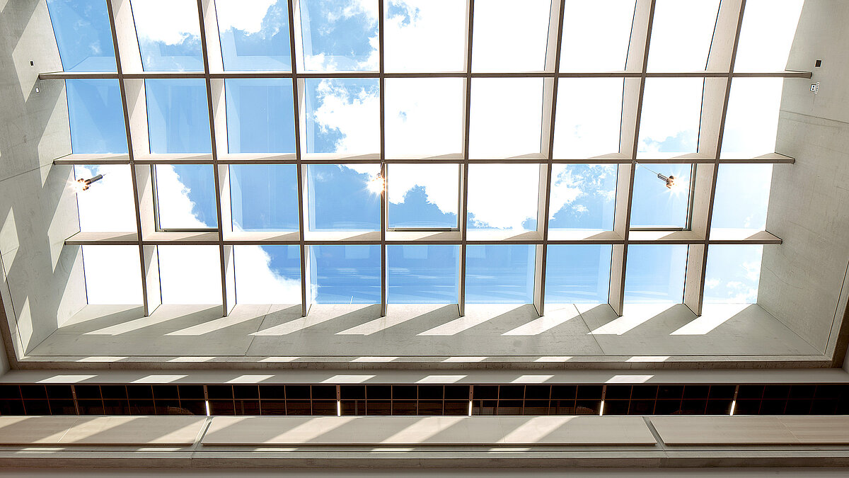 Glasdach PR60 Passivhaus von LAMILUX im Willibald-Gluck-Gymnasium in Neumarkt, mit Blick auf den blauen Himmel und Sonnenstrahlen.