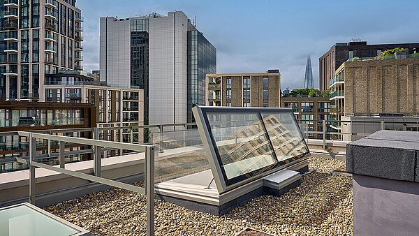 LAMILUX Flachdach Ausstieg auf dem Dach der Mulberry Academy London, umgeben von Kiesbelag und moderner Architektur, im Hintergrund das Hochhaus The Shard.