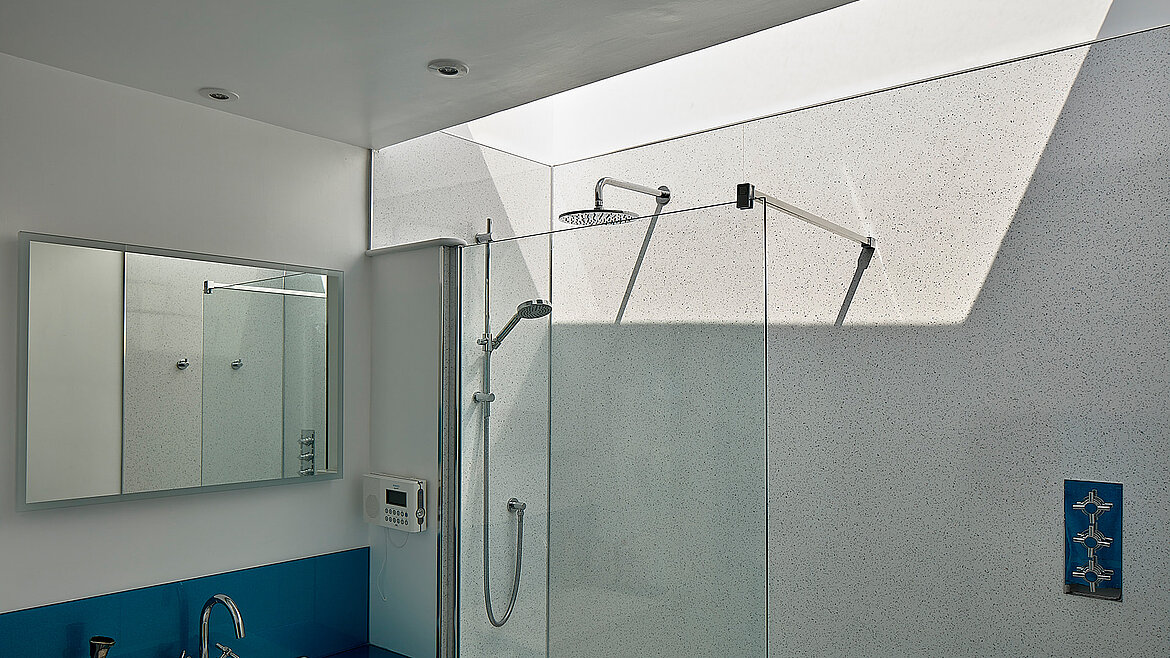 Modernes Badezimmer mit großer Dusche und Tageslichteinfall durch ein schräges Oberlicht.