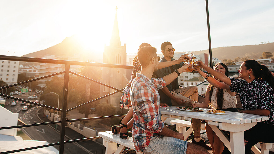 Freunde stoßen auf einer Dachterrasse bei Sonnenuntergang an.