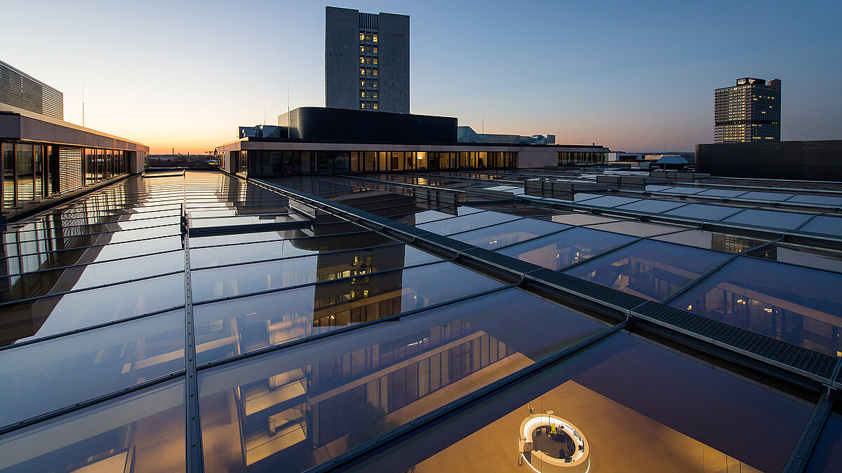 Glasdach des FGS Campus bei Sonnenuntergang mit reflektierenden Glasflächen und modernem Gebäude im Hintergrund.
