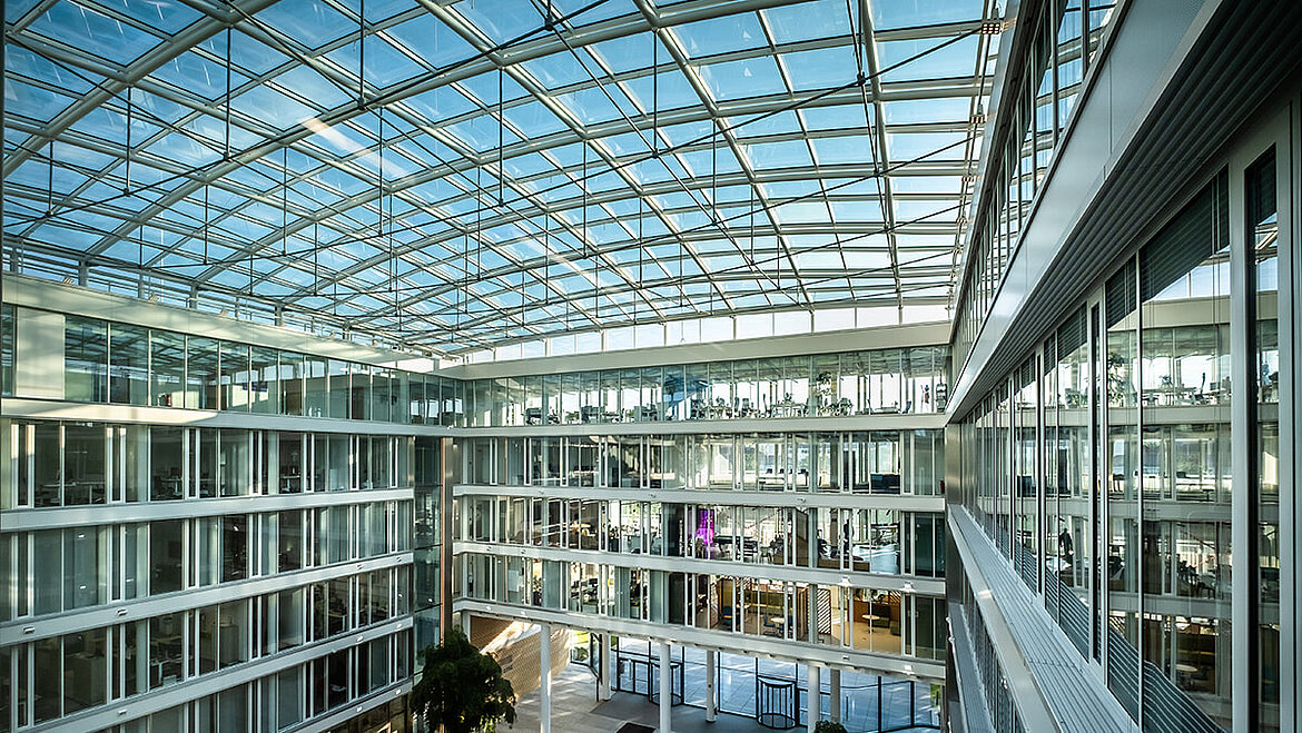 Modernes Atrium des Bürogebäudes Newton der TÜV Süd Gruppe mit Glasdach und großen Glasfassaden.