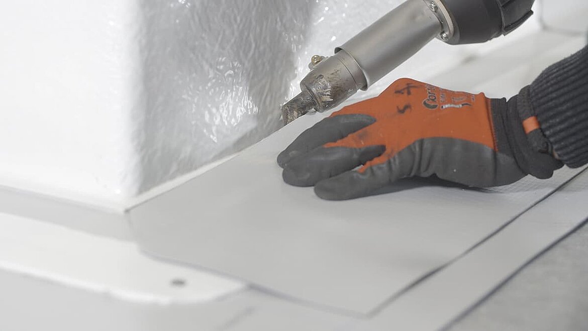 Hand mit Schutzhandschuhen verschweißt Dachfolie mit Heißluftgerät.