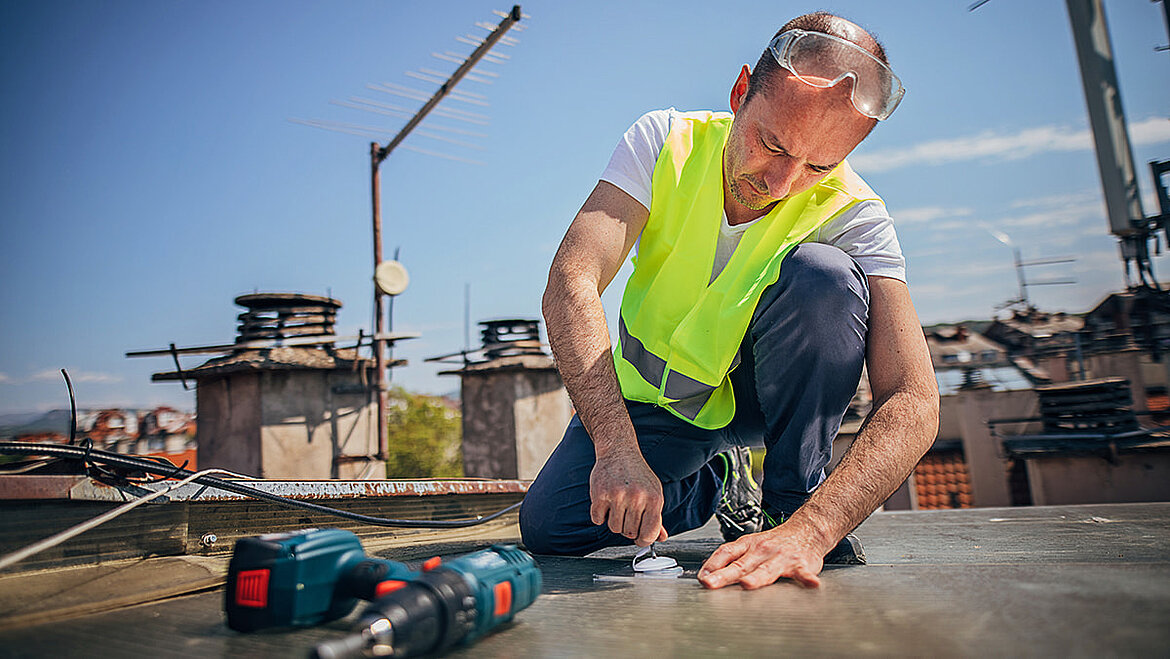 Bauarbeiter mit Warnweste arbeitet mit Werkzeug auf Dach 