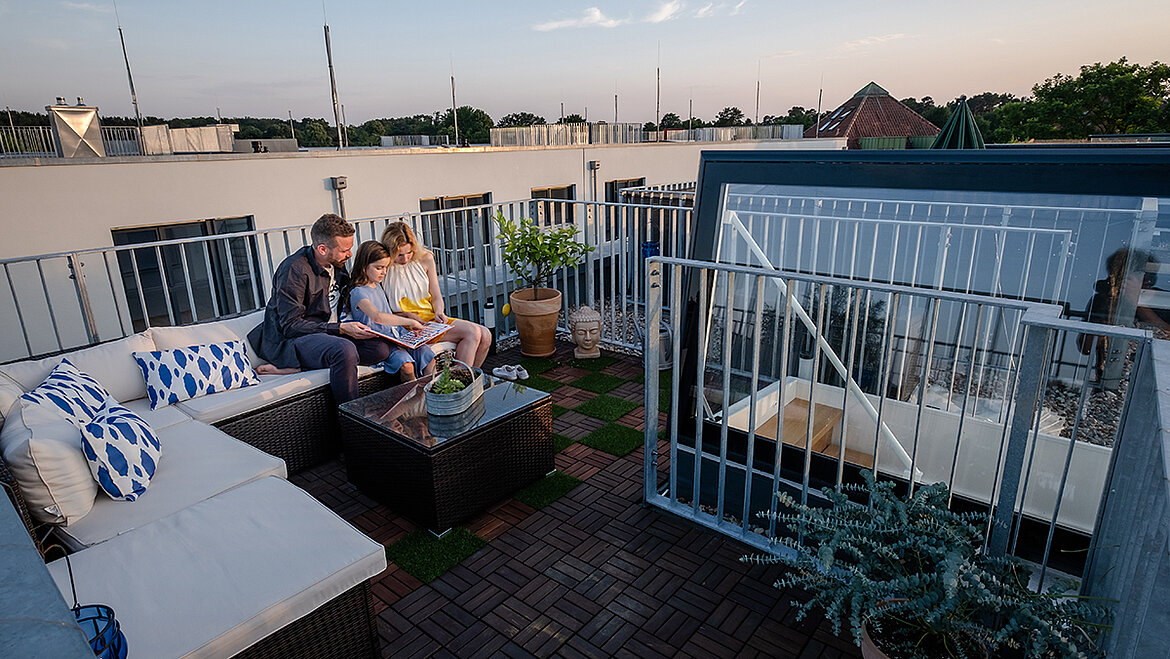 Familie sitzt bei Sonnenuntergang auf der Dachterrasse von ihrem Townhouse in Berlin mit Flachdach Ausstieg.