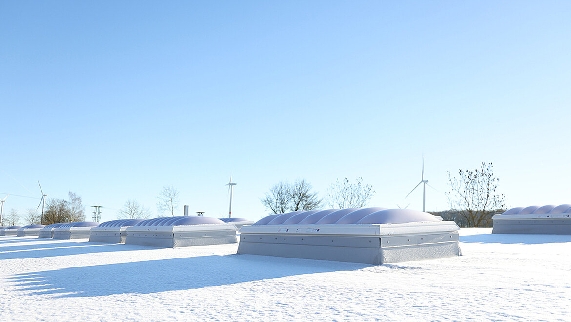 Flachdach mit Schneedecke und Lichtkuppeln bei sonnigem Wetter.