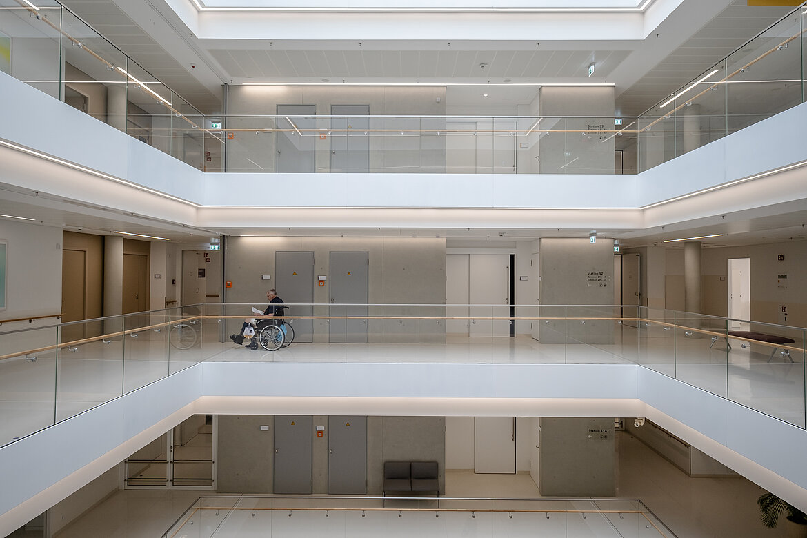 Modernes, lichtdurchflutetes Atrium mit mehreren Etagen und Glasgeländern.