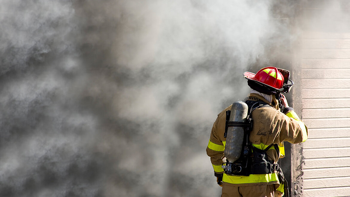 Feuerwehrmann vor brennendem Gebäude mit Brandrauch