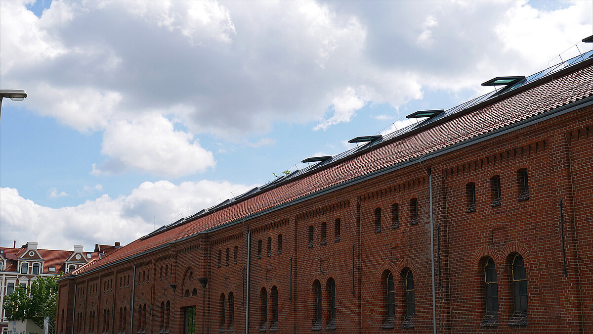 Rotes Backsteingebäude der Leibniz-Universität Hannover mit modernem Glasdach und geöffneten Oberlichtern unter bewölktem Himmel.