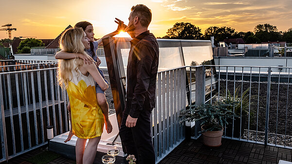 Familie auf der Dachterrasse eines Townhouses in Berlin bei Sonnenuntergang, neben einem Flachdach Ausstieg mit Glasabdeckung.