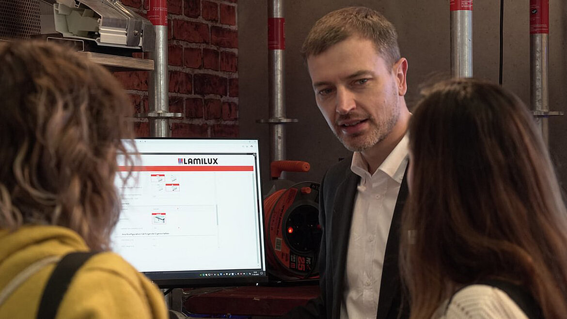 Carste Ficker erklärt zwei Frauen die LAMILUX Planungsunterstützung auf einem Monitor.