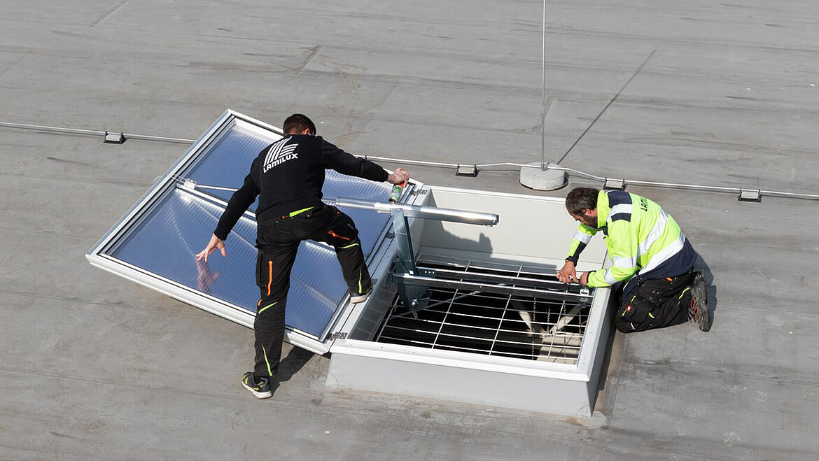 Zwei Menschen bauen an geöffneter Lichtkuppel auf dem Dach