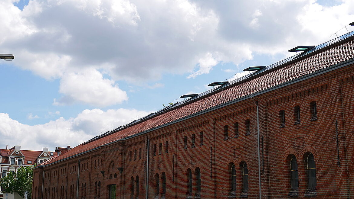Ziegeldach einer historischen Industriehalle mit Oberlichtern unter blauem Himmel.