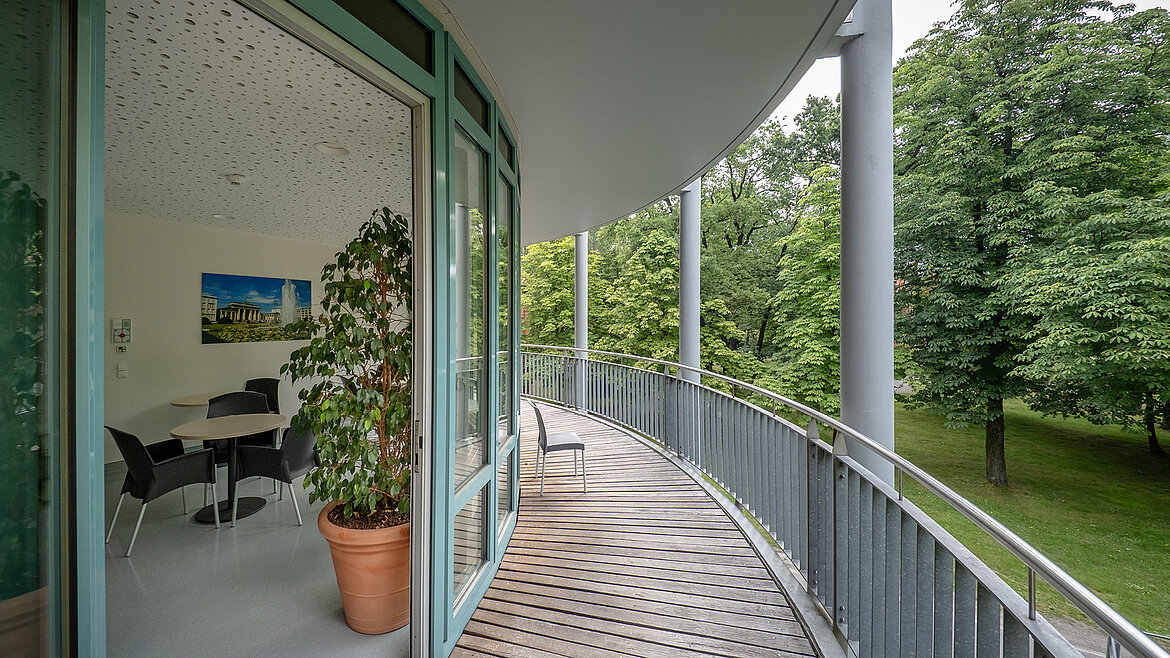 Geschwungener Balkon mit Blick ins Grüne, angrenzend an ein modernes Büro mit Glasfront.