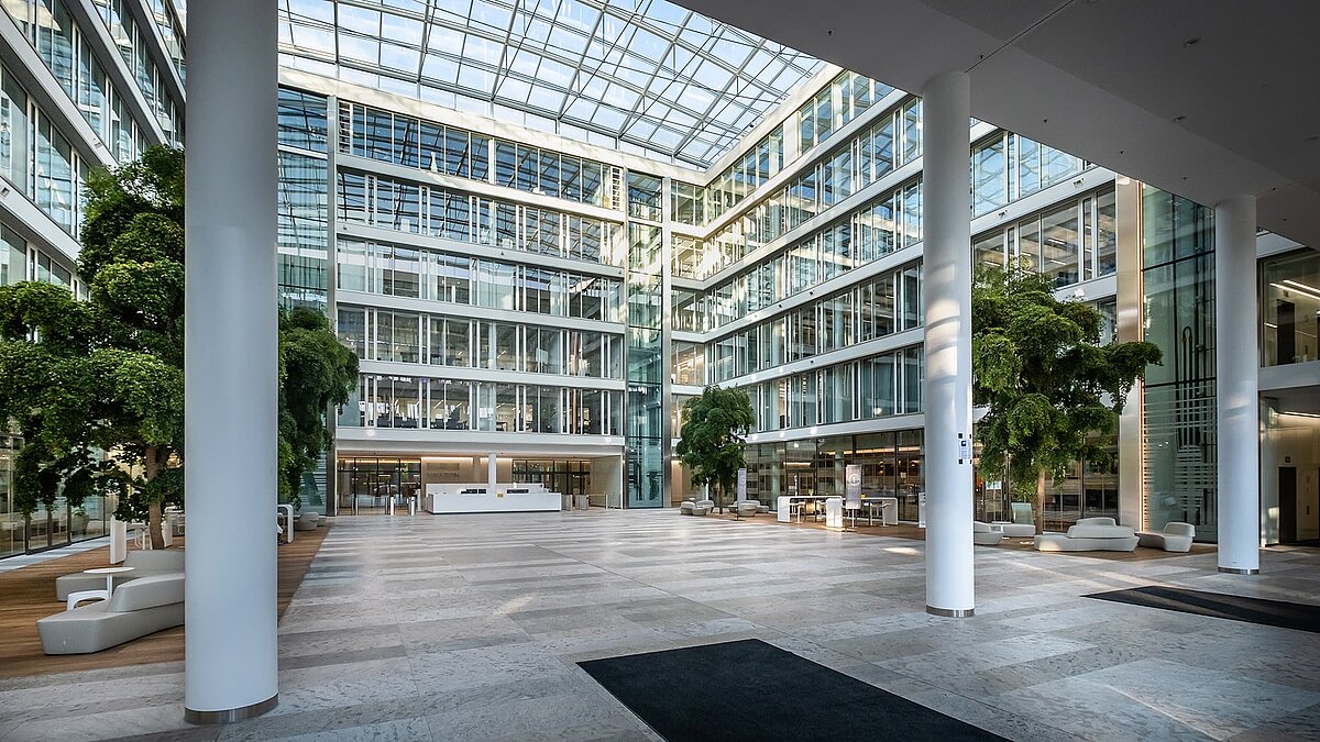 Großes Atrium im Bürogebäude Newton der TÜV Süd Gruppe in München mit Glasdach, modernen Säulen und bepflanzten Innenbereichen.
