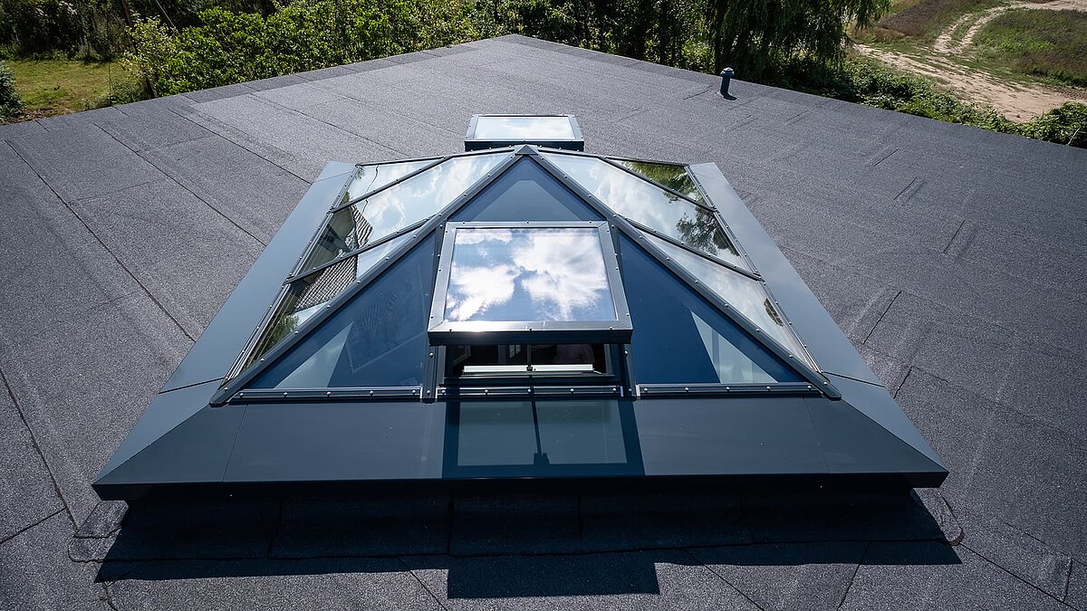 Glaspyramide auf dem Flachdach eines Einfamilienhauses in Wichmannsdorf mit reflektierendem Himmel und geöffnetem Lüftungsfenster.