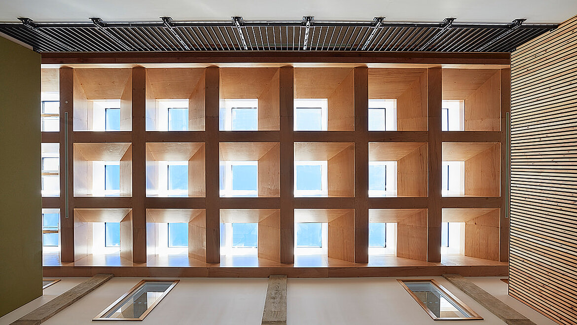 Innenansicht eines Atriums mit Holzlamellen und quadratischen Fensteröffnungen