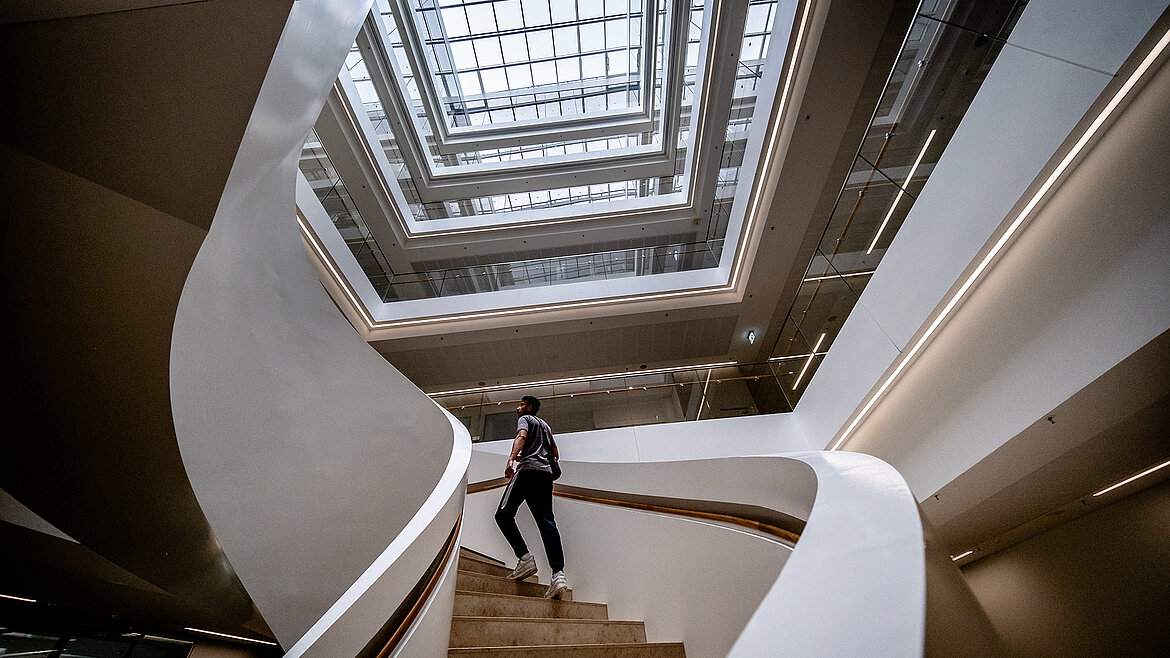 Person geht eine moderne Wendeltreppe in einem lichtdurchfluteten Atrium hinauf.