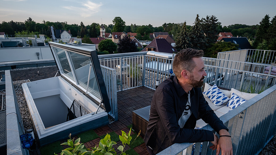 Mann genießt den Ausblick von einer modernen Dachterrasse bei Sonnenuntergang.