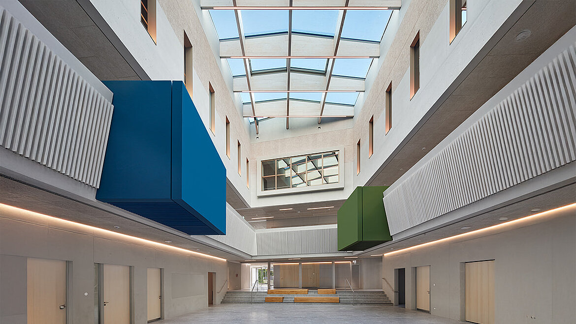 Modernes Atrium mit Oberlicht, wellenförmigen Wänden und farbigen Box-Elementen.