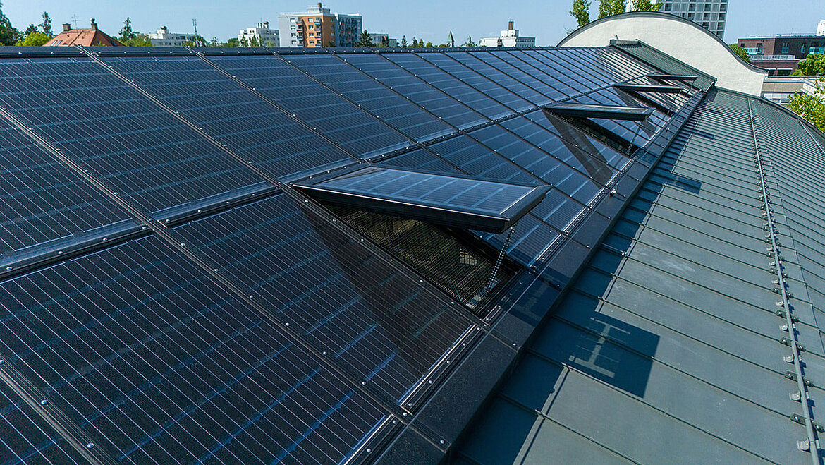 Ein langes Dach eines städtischen Gebäudes mit transparenten Solarmodulen.