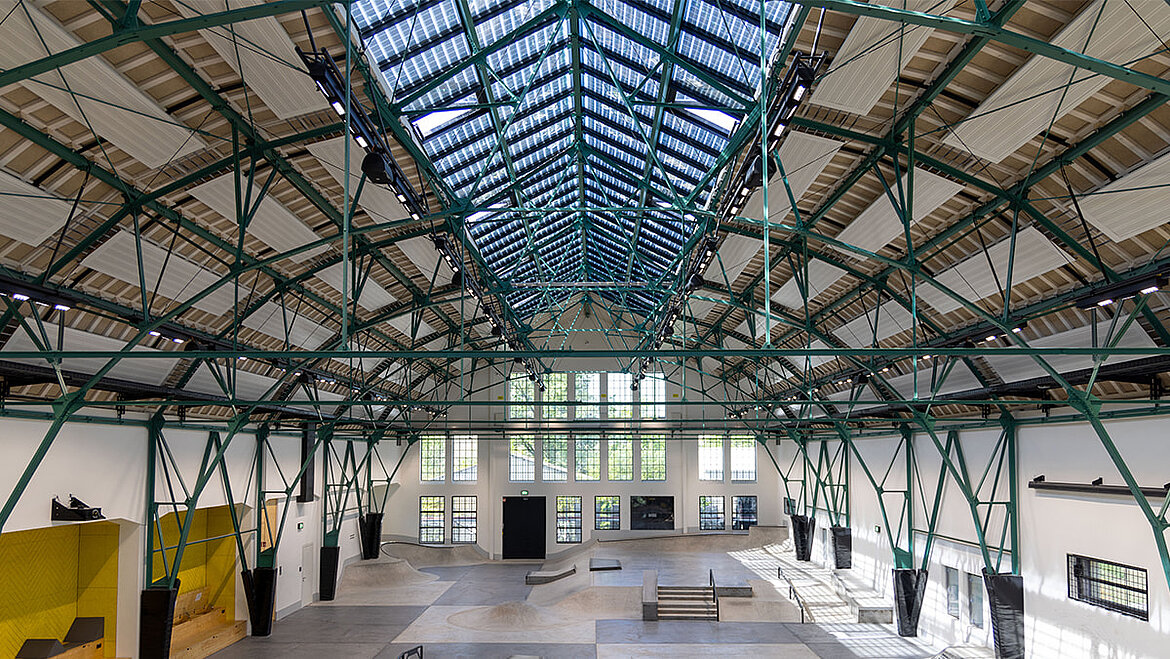 Industriehalle mit historischem Stahlträgerdach und modernen Oberlichtern.