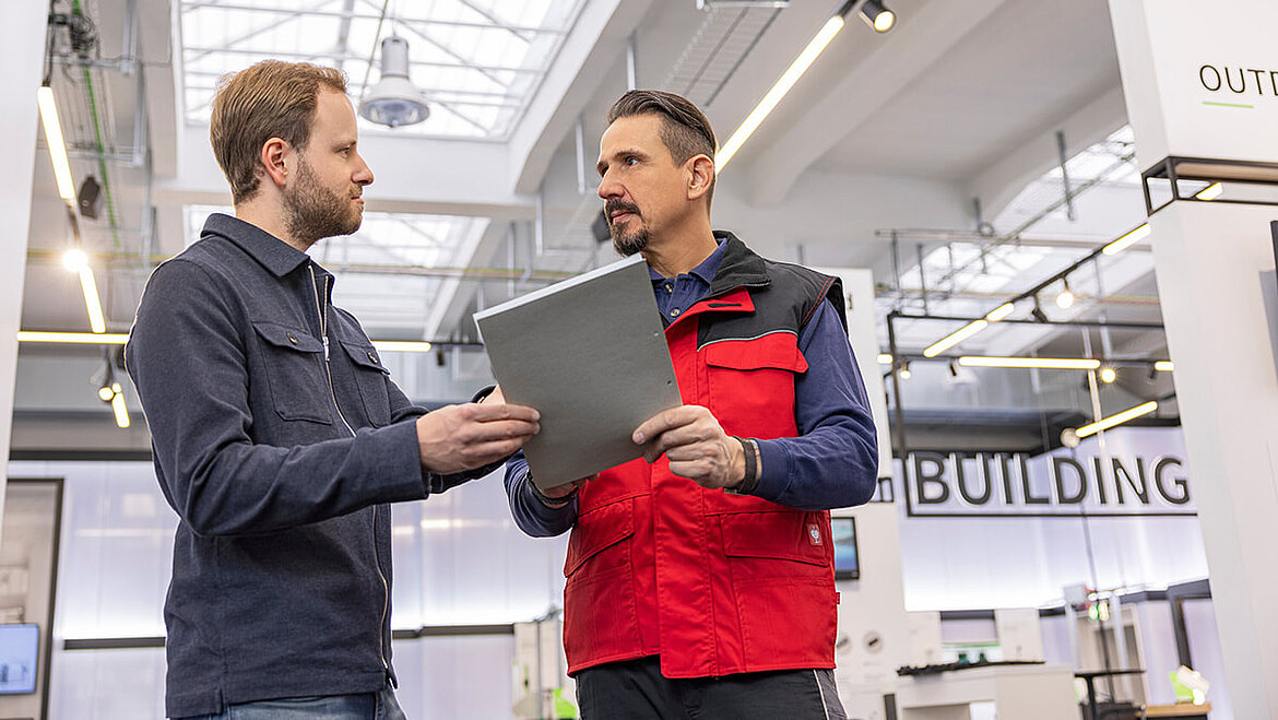 Zwei Männer besprechen Unterlagen in einer modernen Industriehalle