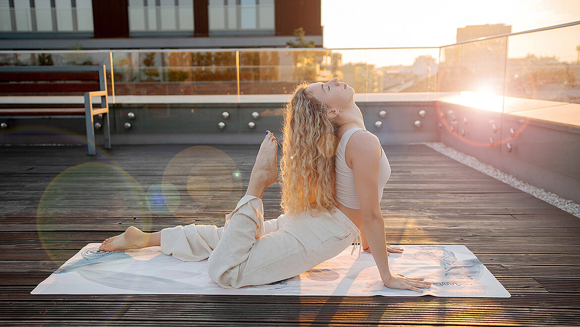 Frau praktiziert Yoga auf einer Dachterrasse bei Sonnenuntergang.