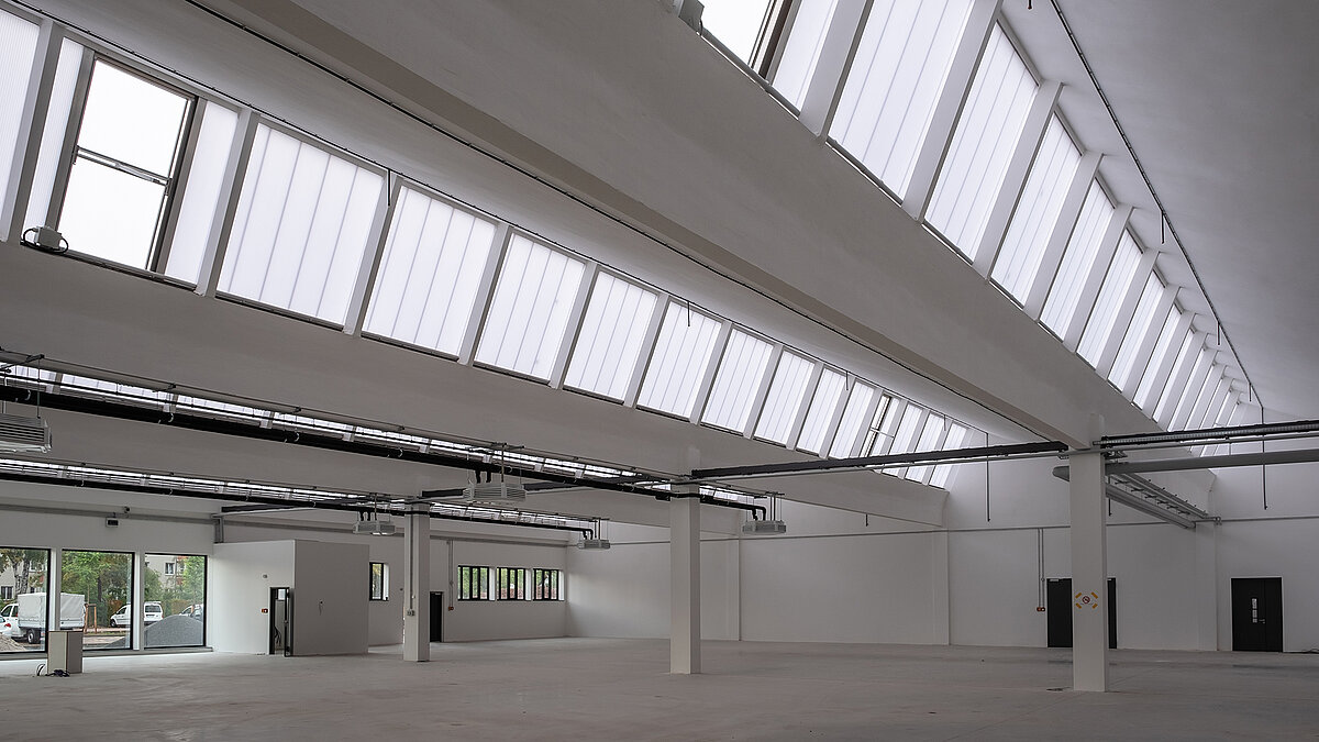 Innenansicht des alten Postbahnhofs Leipzig, saniert mit großen Glasdachfenstern und moderner weißer Architektur.