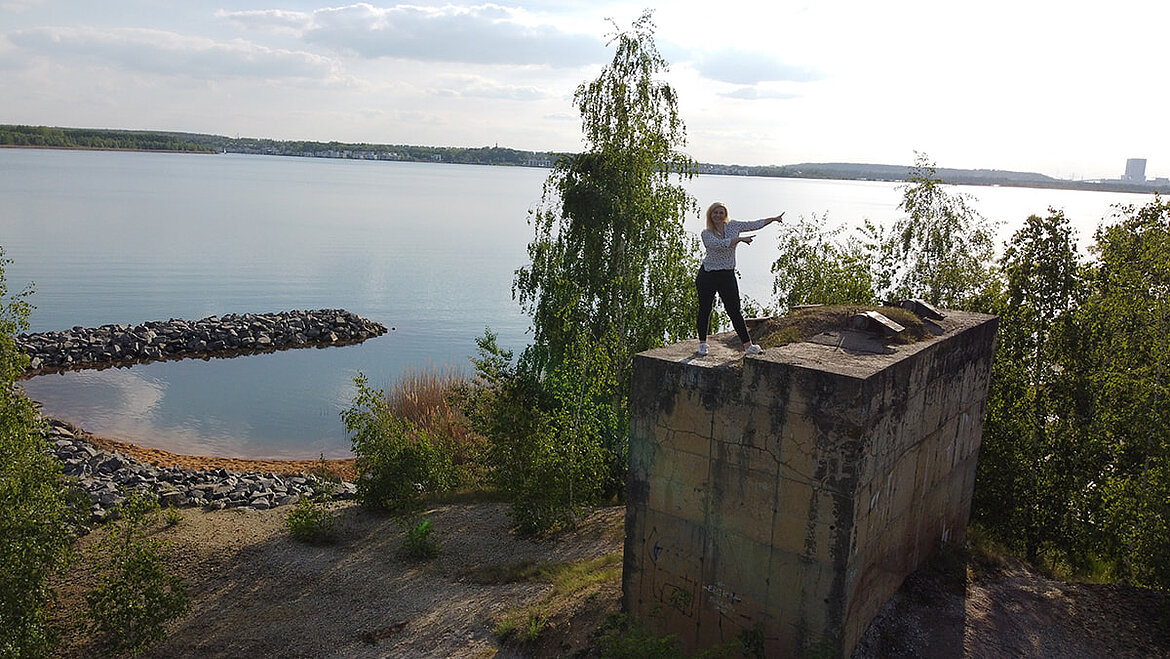 Steffi steht auf dem Betonfundament des DIY-Leuchtturms, am See umgeben von Bäumen