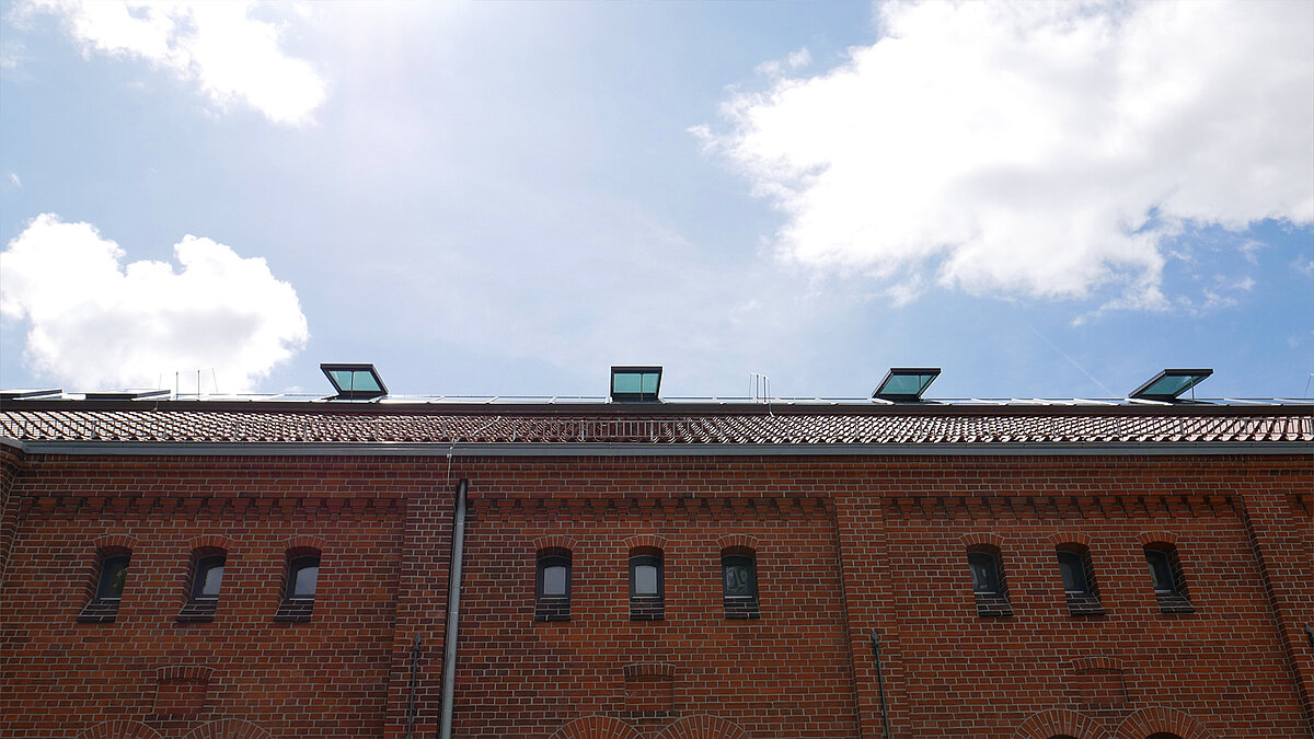 Ziegelsteinfassade der Leibniz-Universität Hannover mit Glasdach-Elementen auf dem Dach unter blauem Himmel.