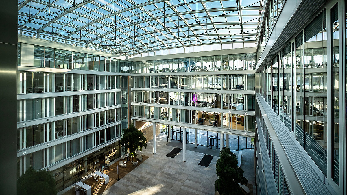 Modernes Atrium des Bürogebäudes Newton der TÜV Süd Gruppe mit Glasdach und großen Glasfassaden.