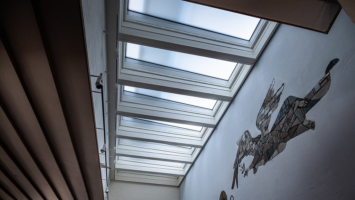 Innenansicht der Pauluskirche in Traunreut mit LAMILUX Flachdachfenstern FE und einer großen Wandmosaik-Darstellung.