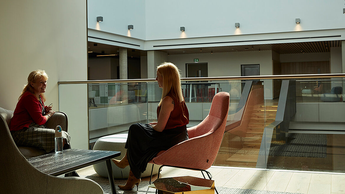 Zwei Frauen unterhalten sich in einer modern gestalteten, lichtdurchfluteten Lounge mit Oberlicht.
