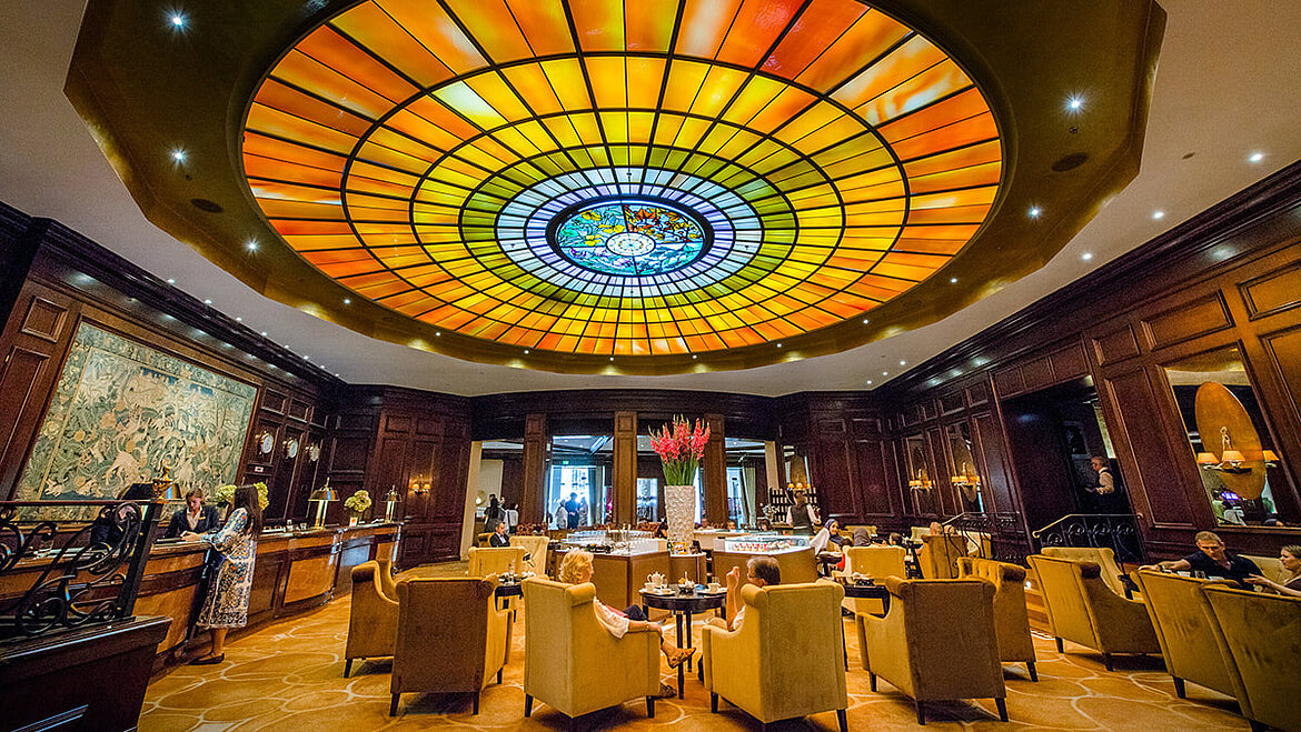 Indirekt mit Tageslicht beleuchtetes Glasmosaik in der Hotellobby des Vier Jahreszeiten in München Glasdachpyramide beleuchtet indirekt ein rundes Glasmosaik über Hotellobby | insights by LAMILUX