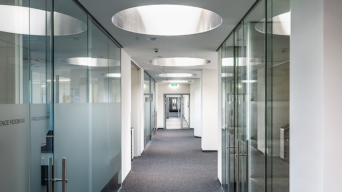 Moderner Büroflur mit Glastrennwänden und runden Flachdach Fenster für natürliches Tageslicht.