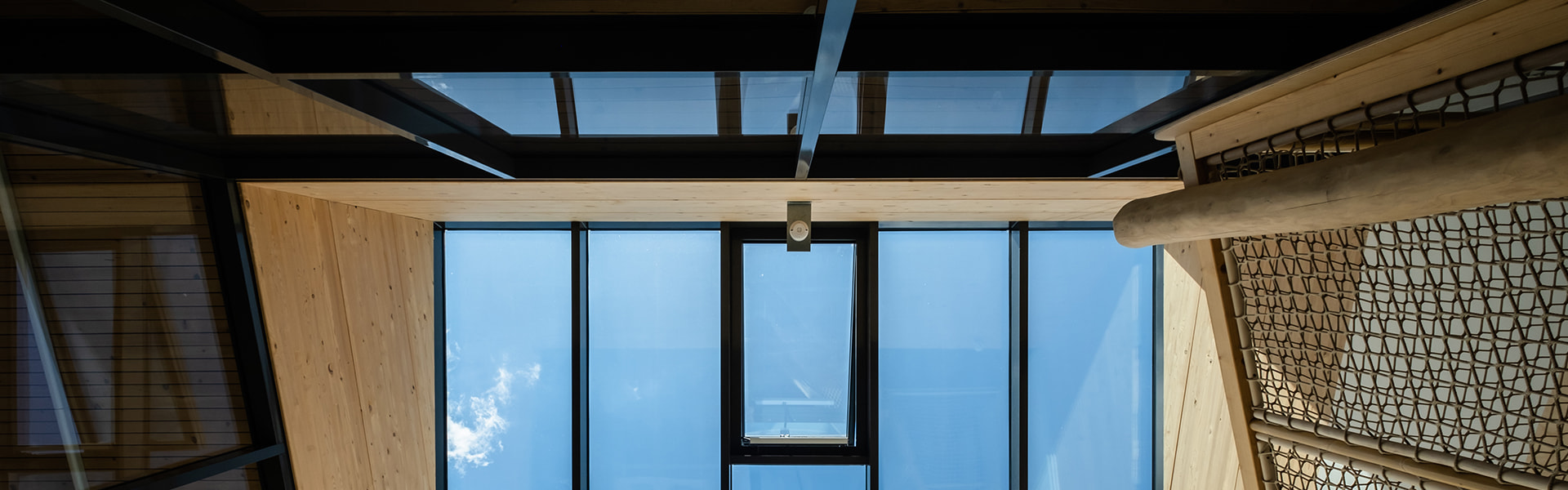 Blick nach oben durch ein modernes Glasdach mit blauem Himmel.